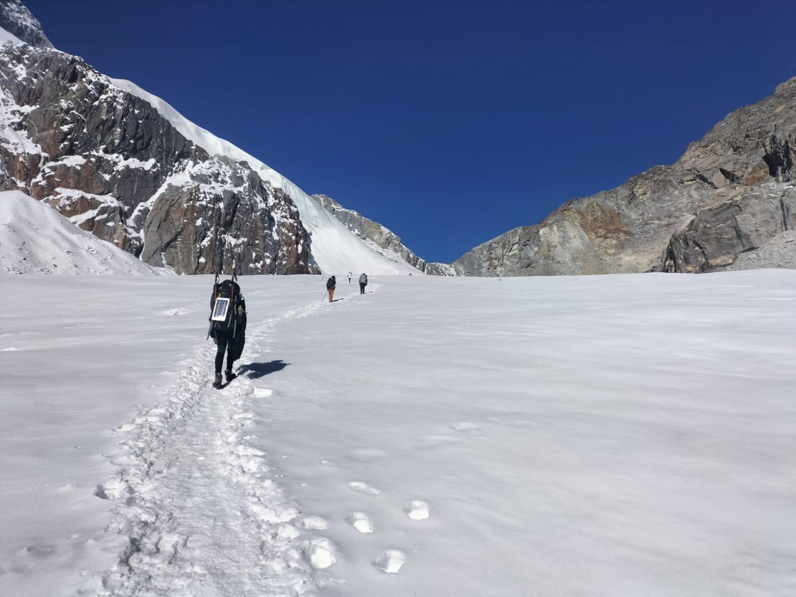 A lone figure carrying a large backpack crosses an isolated snowy pass